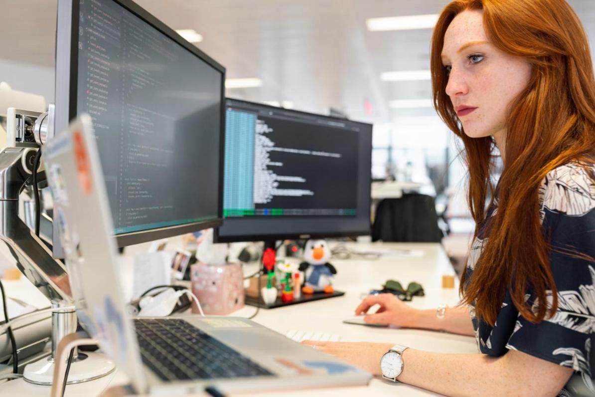 Engenheira de software trabalhando com código em vários monitores